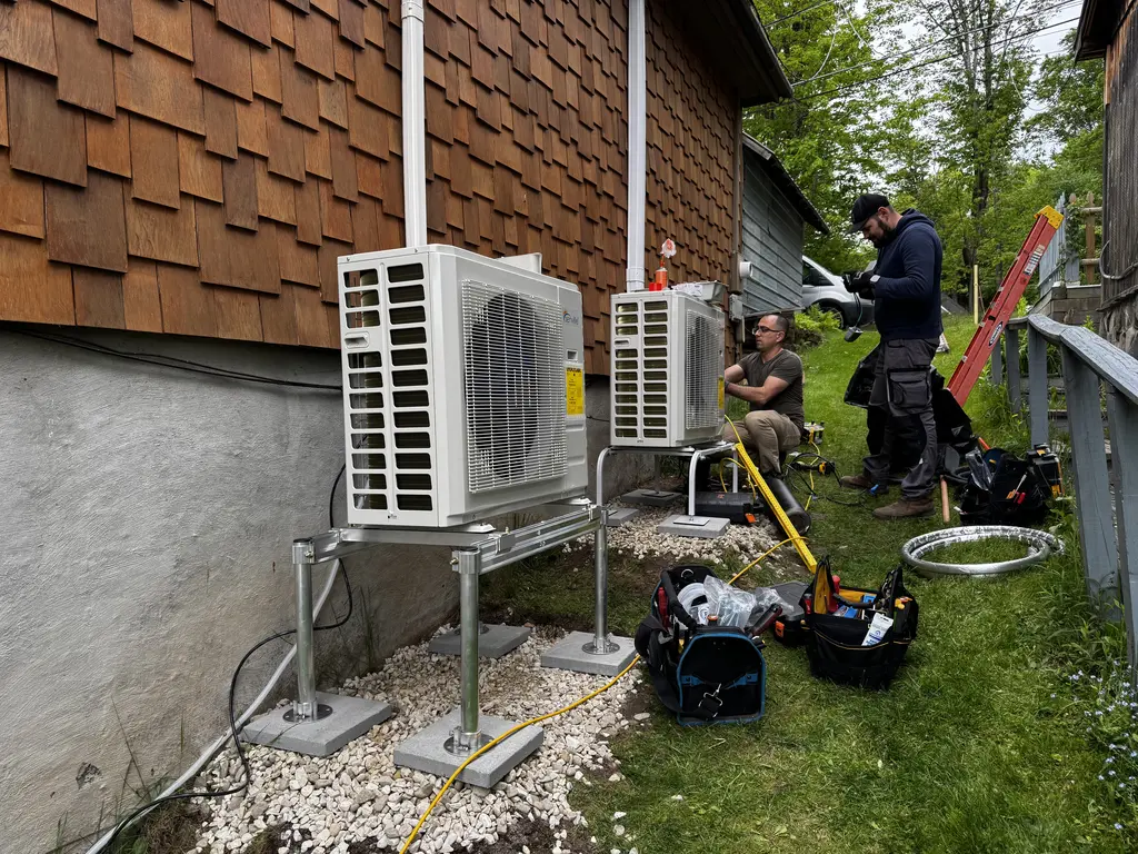 Two HVAC technicians working outside a residential building in the Capital District, NY, assembling tool bags and equipment near a pair of newly Senville condensers installed on a stands in East Greenbush , ny