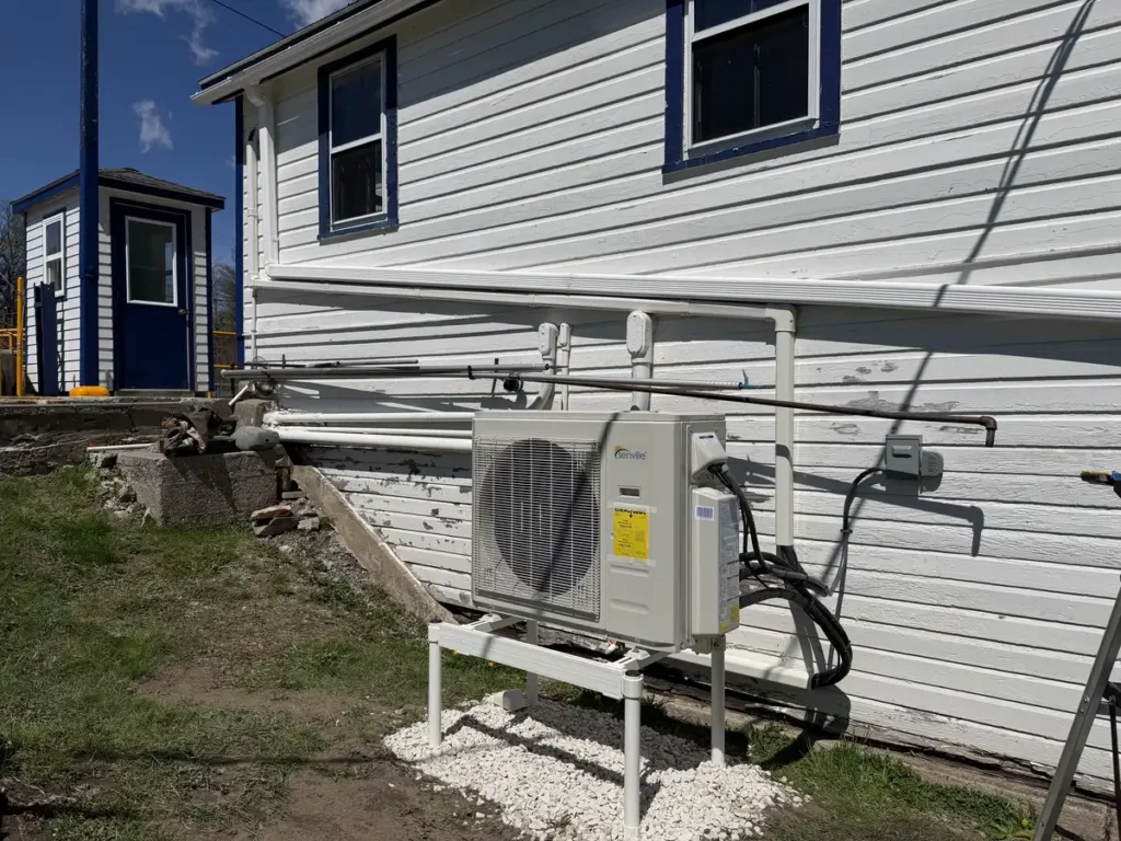 Astello LLC brand-new Senville multi-zone mini-split heat pump condenser cleanly installed on a snow stand over a gravel bed outside a home in Troy, NY.