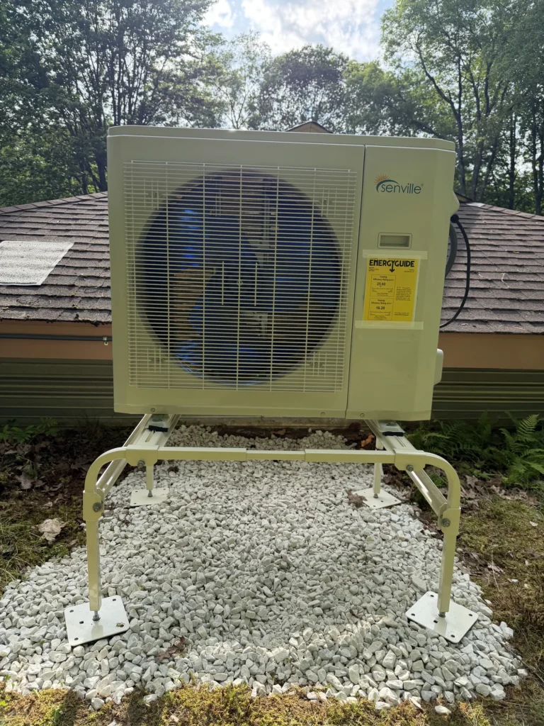 Astello LLC installation of a Senville heat pump condenser on a ground stand with white decorative gravel in a residential backyard in the Capital District, NY.