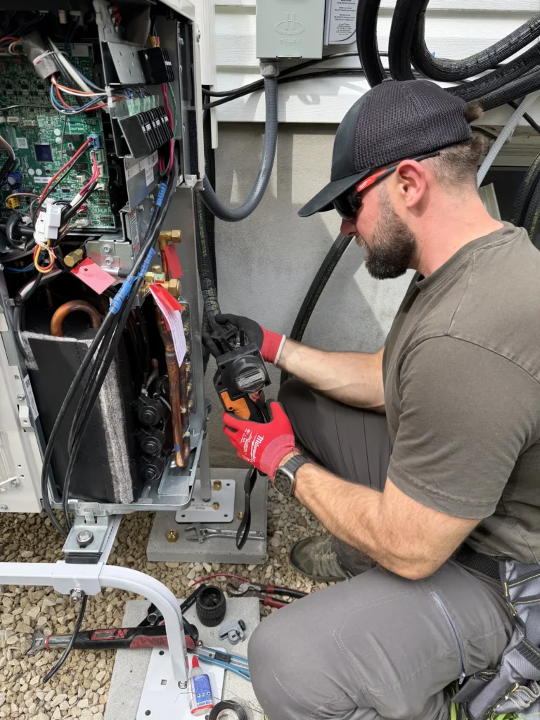 An Astello LLC technician uses a power press tool to connect copper refrigerant lines on an open ductless mini-split heat pump condenser during an outdoor installation. Astello LLC, Albany, NY
